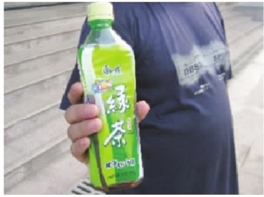 周先生拿著內含黃色不明沉淀物的半瓶康師傅綠茶。 周先生拿著內含黃色不明沉淀物的半瓶康師傅綠茶。